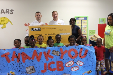 (From left) Steve Vernon, JCB VP o finance, and Thom Peebles, JCB VP of marketing, present a $100,500 check to The Lady Bamford Center children, staff and Tammy Mixon, executive director of the Wesley Community Centers.