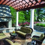 A custom stone fireplace with a limestone mantle and hearth accent this intimate seating area beneath the wooden pergola.
