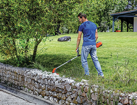 Person trimming with robotic mower in background (Photo: Husqvarna)