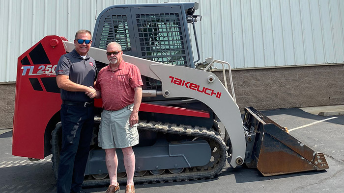 Carl Stickels, Northeast region business manager for Takeuchi-US (left) and Mark Butler, president of Butler Equipment, celebrate the new partnership next to Butler’s personal Takeuchi TL250 compact track loader. (Photo: Takeuchi)