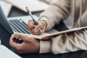 a person holding a pen and writing on a notebook (Photo: PeopleImages / iStock/Getty Images Plus / Getty Images)