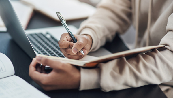 a person holding a pen and writing on a notebook (Photo: PeopleImages / iStock/Getty Images Plus / Getty Images)