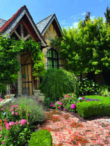 The weeping cherry tree touches the ground, the manicured wisteria covering the roofline is trained to grow and the boxwood is maintained as a continuous hedge with a rounded top. (Photo: Sunline Landscapes)