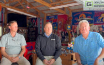 Three men sitting in workshop.