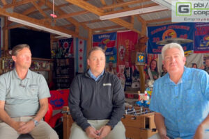 Three men sitting in workshop.