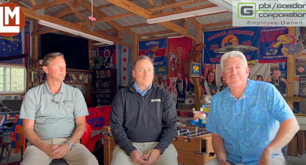 Three men sitting in workshop.